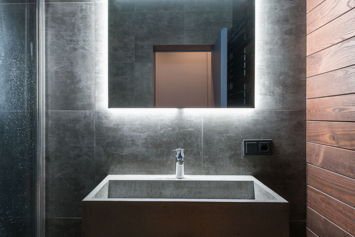 Sleek modern bathroom featuring an illuminated mirror, concrete sink, and elegant gray tiles.