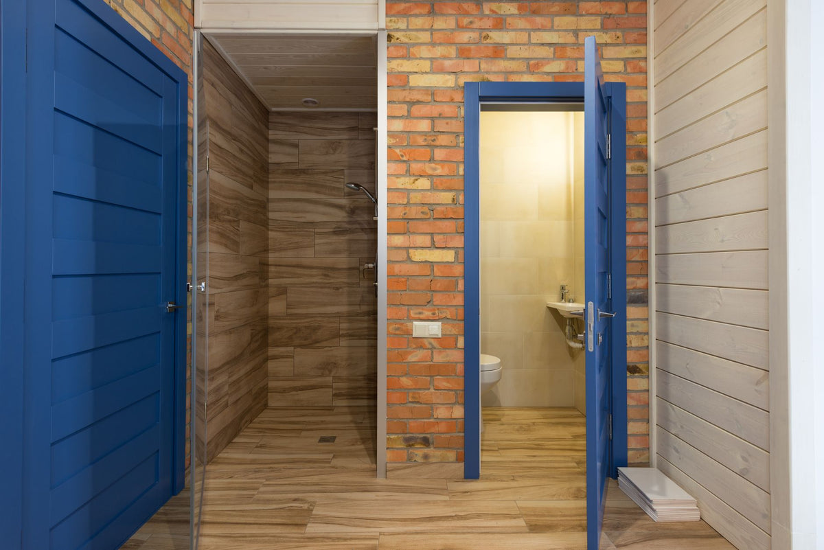 Contemporary bathroom interior with wooden and brick materials, featuring blue doors and a shower area.