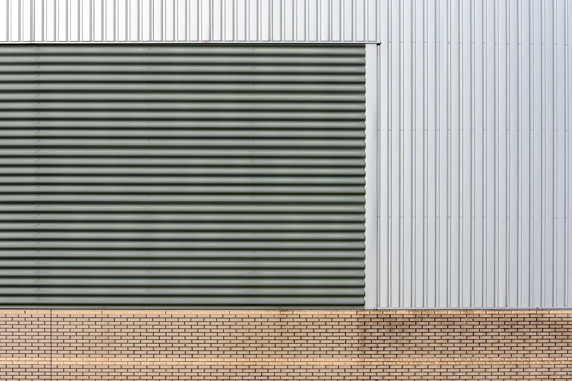 Close-up of industrial building facade with metal siding and brick base, showcasing slick and modern design.