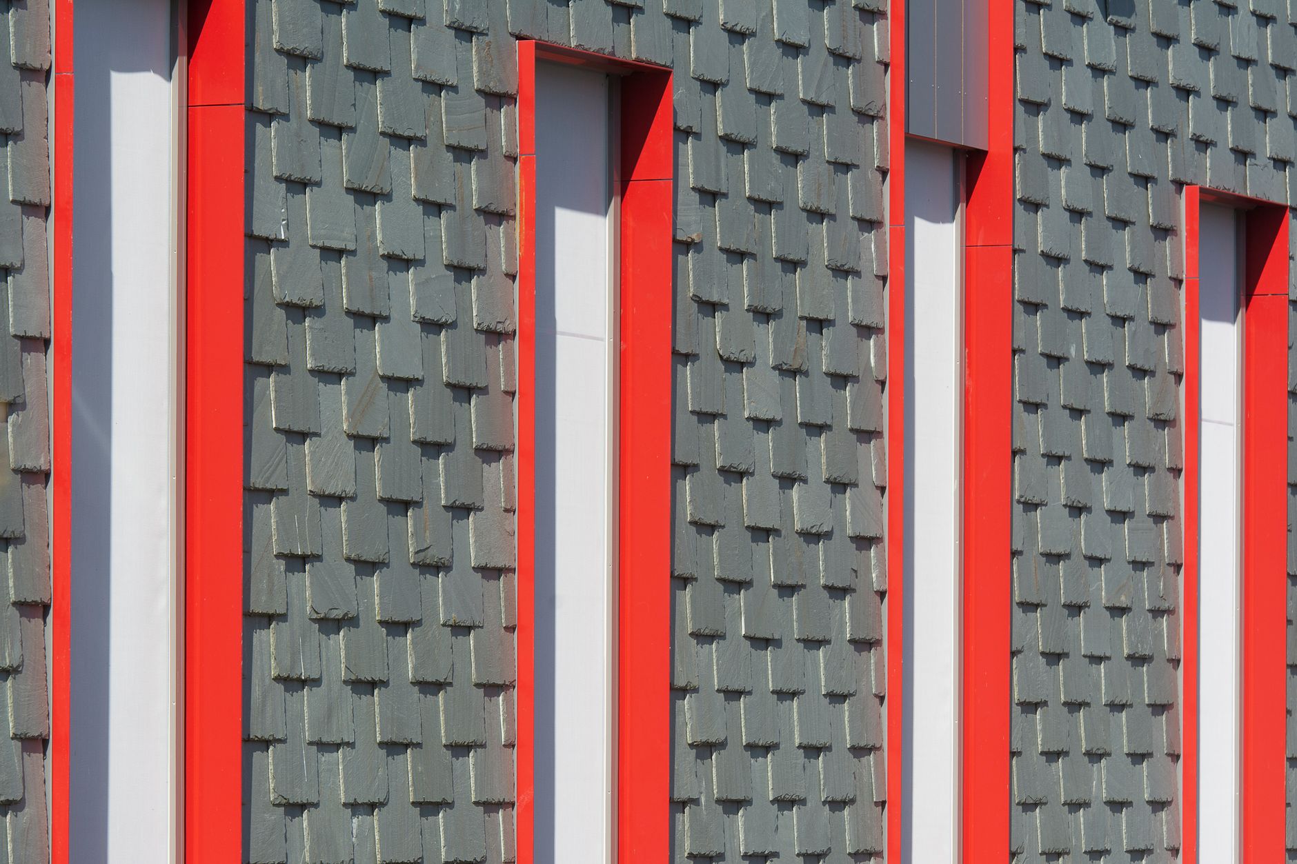 Close-up of a modern building facade with red window frames and textured panels.