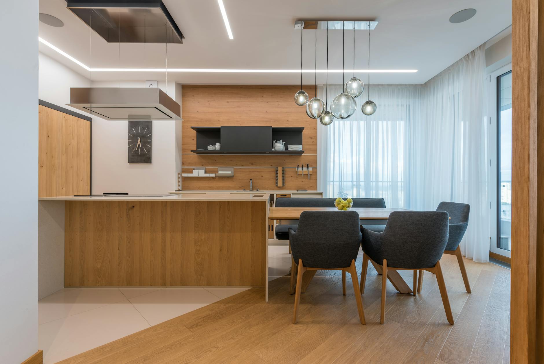 Interior of contemporary kitchen with wooden furniture and floor and dining table with soft chairs in cozy apartment