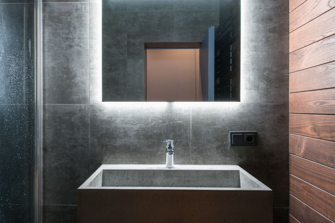 Sleek modern bathroom featuring an illuminated mirror, concrete sink, and elegant gray tiles.