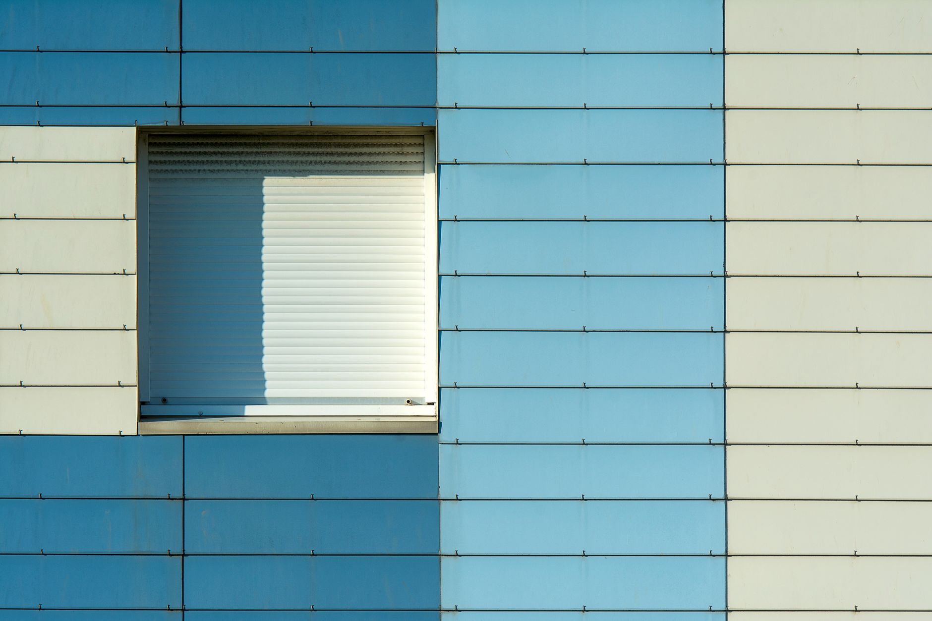 Close-up of a blue and white building facade with a closed window shade.
