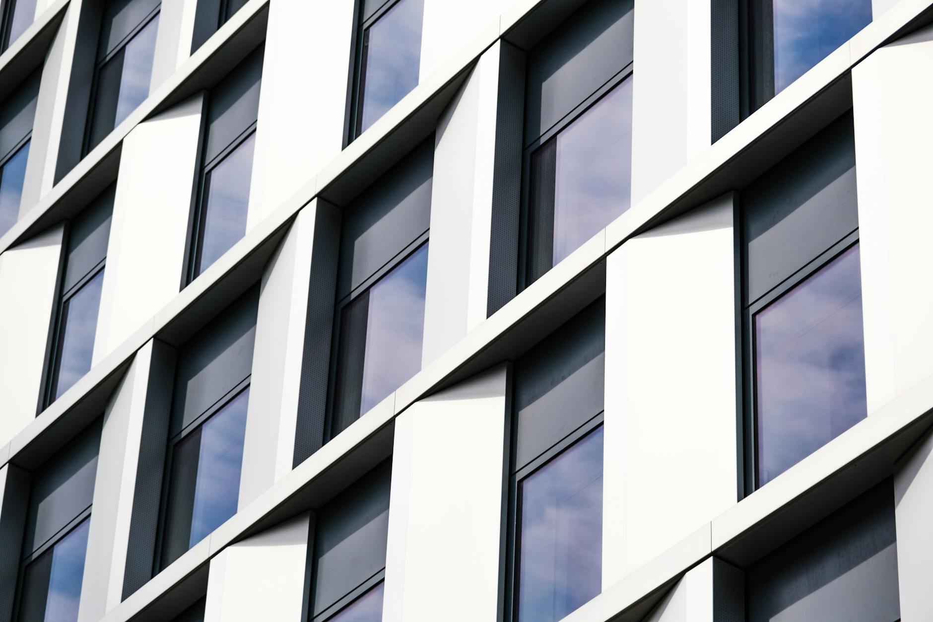 Diagonal view of a modern building facade with reflective glass windows, casting sky reflections.