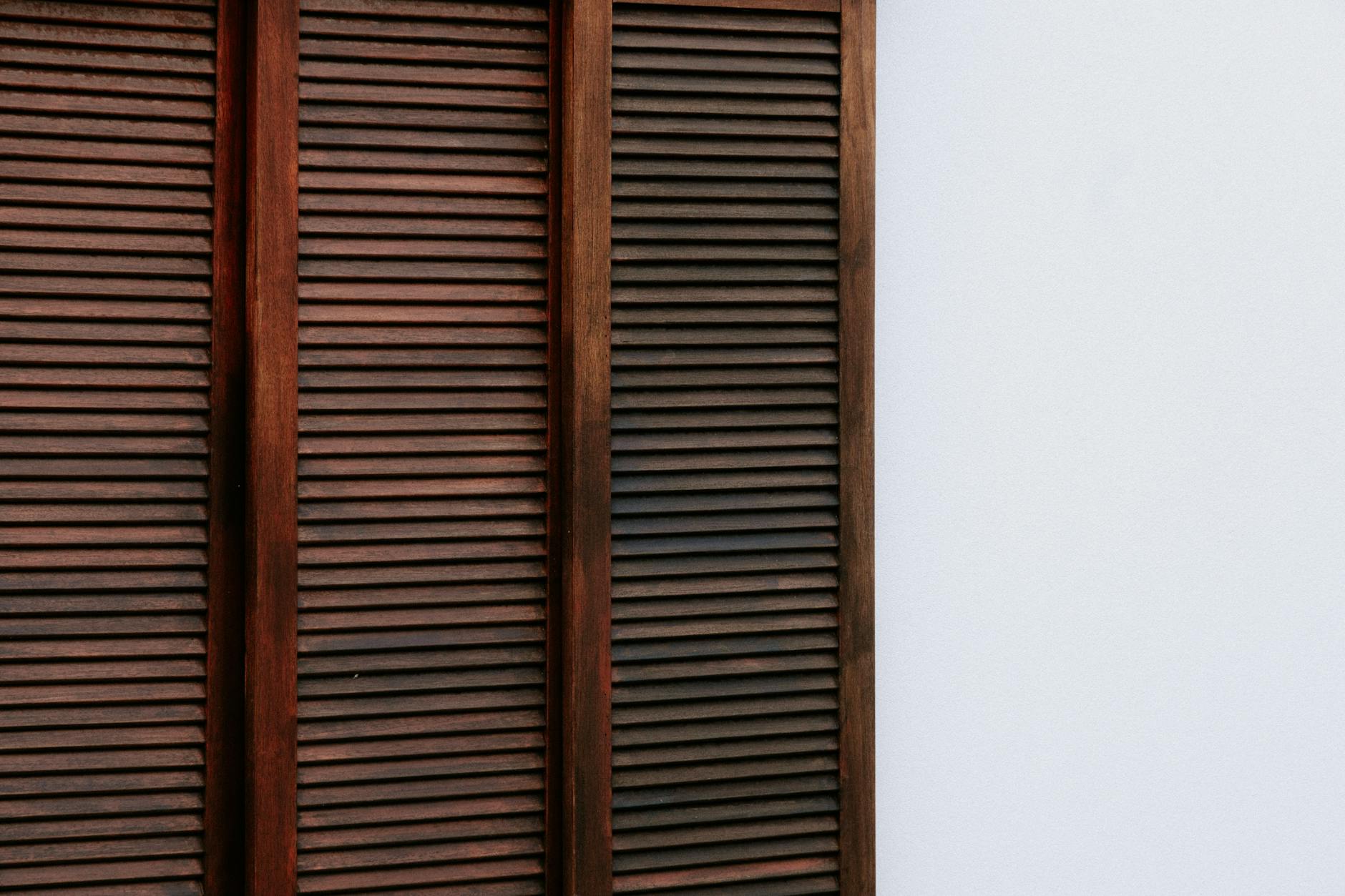 Close-up of dark wooden shutters contrasting a white wall, perfect for design inspiration.
