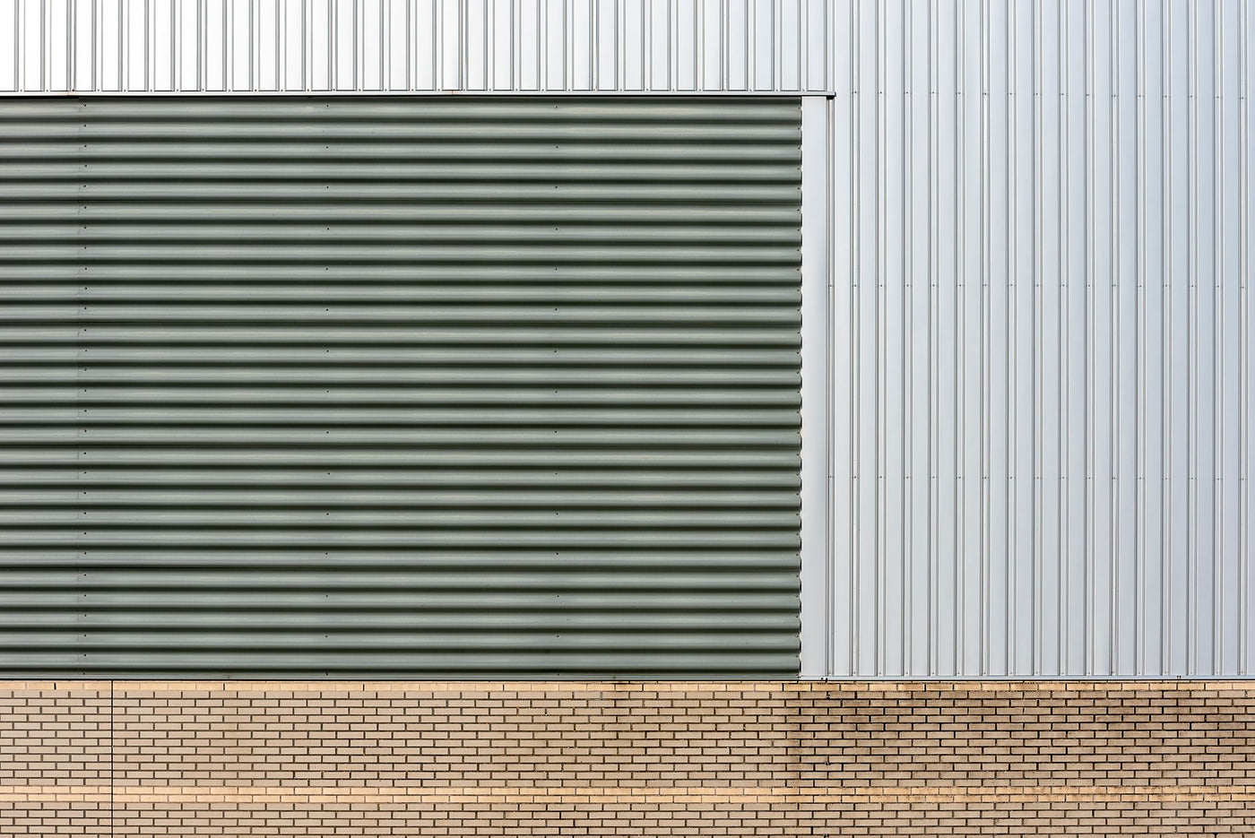 Close-up of industrial building facade with metal siding and brick base, showcasing slick and modern design.