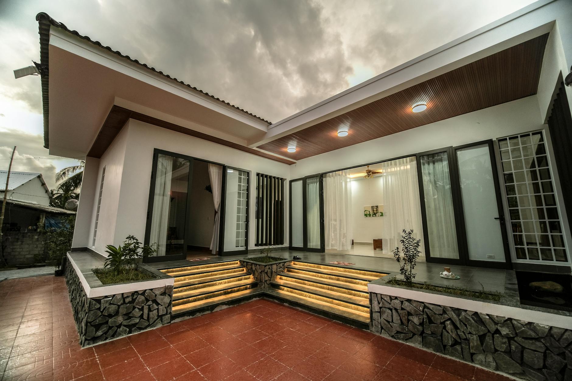 Contemporary one-story house exterior with large glass doors and lit steps during overcast weather.